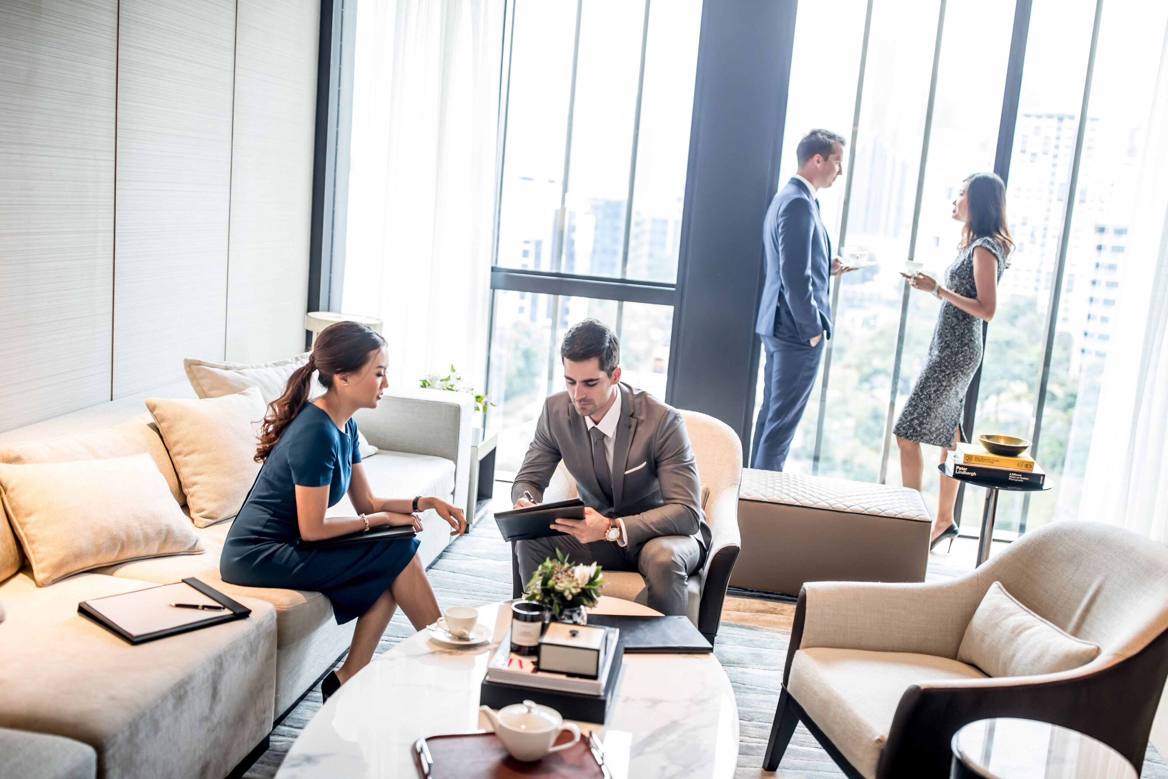 Une chambre d’hôtel moderne dotée d’une grande fenêtre, d’un canapé, d’une table basse avec une théière et d’un ordinateur portable.