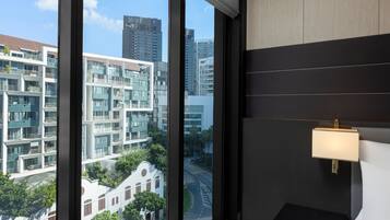 Quarto de hotel moderno com grandes janelas que oferecem vista para edifícios e rua ao redor.