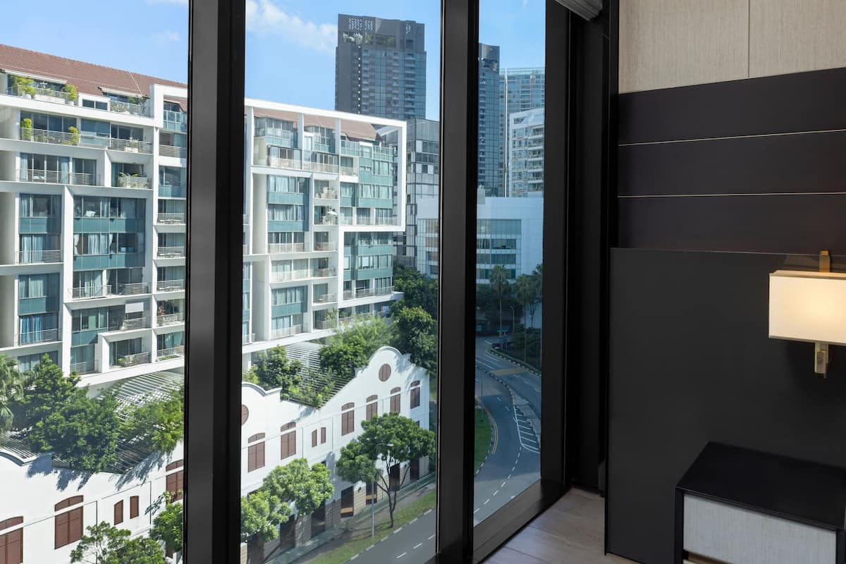 Una habitación de hotel moderna con ventanas amplias que ofrecen vista a un paisaje urbano, incluyendo edificios altos y una calle.