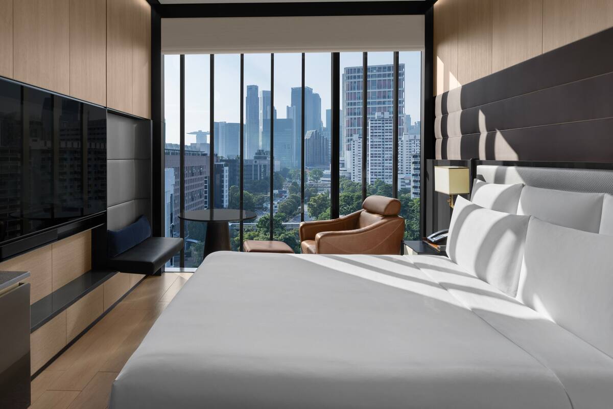 Habitación de hotel moderna con una cama grande, una zona de estar con una silla, una mesita y un televisor montado en la pared.