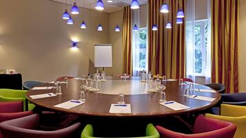 Un salón de conferencias con una mesa redonda, sillas coloridas y lámparas colgantes azules.