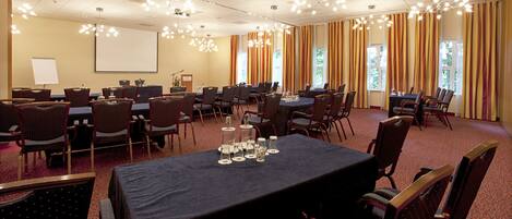 A conference room with multiple tables and chairs, a projector screen, and a large window with curtains.