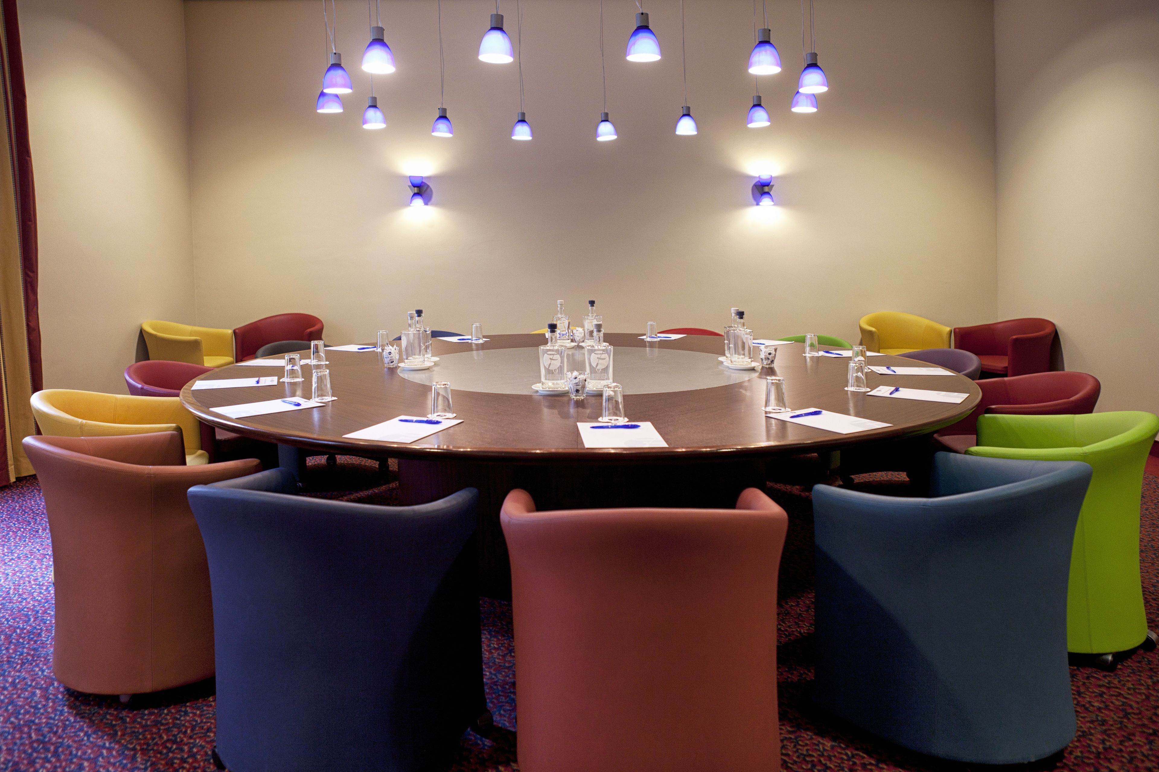 A conference room with a round table, colorful chairs, and pendant lighting.