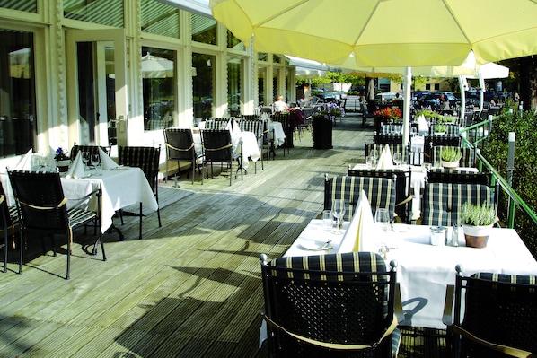 An outdoor dining area with tables and chairs, large umbrellas, and potted plants.