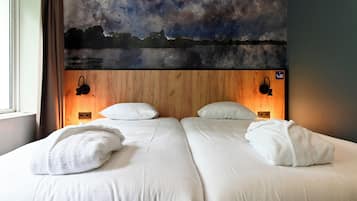Cama doble con sábanas y almohadas blancas, cabecera de madera con un cuadro y dos lámparas fijadas a la pared.