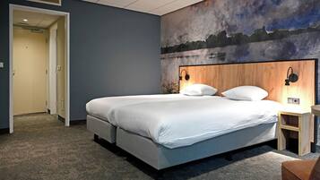 Una habitación de hotel con una cama grande, un cabecero con decoración en la pared, una mesita de noche y una puerta que da a otra habitación.