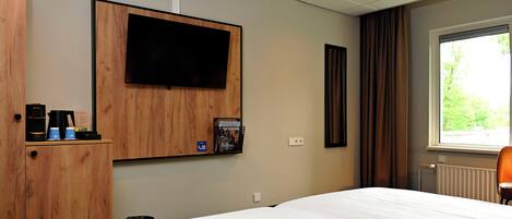 A hotel room with a bed, a mounted television, a coffee machine, and a window with curtains.