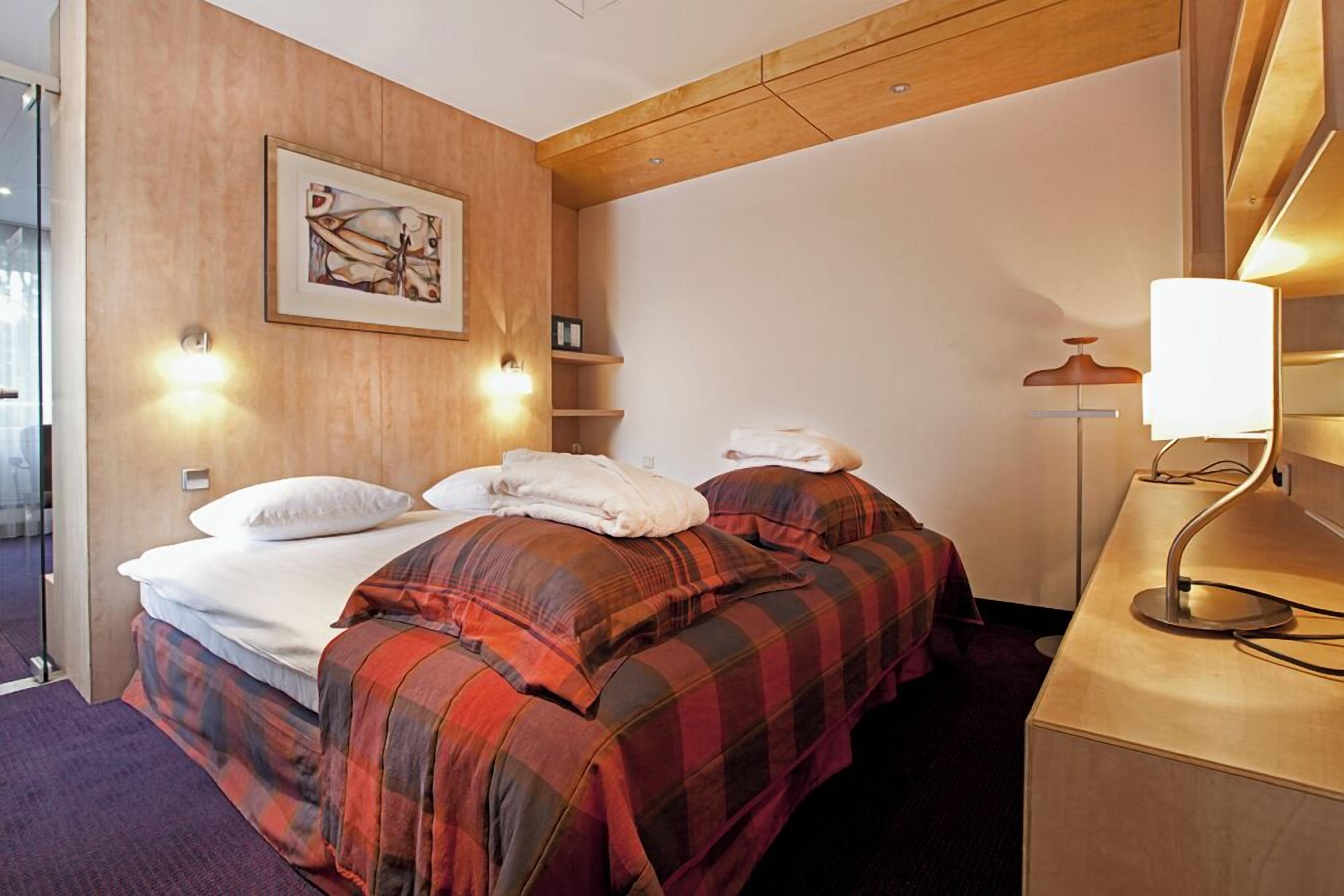 A hotel room with a bed, two bedside tables, a lamp, and a painting on the wall.