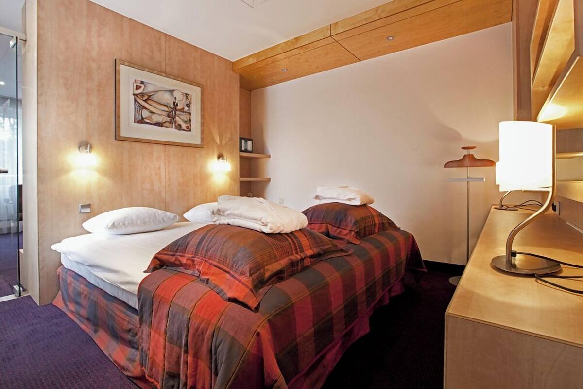 A hotel room with a bed, two bedside tables, a lamp, and a painting on the wall.