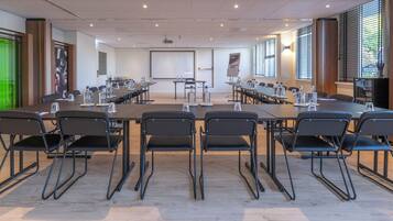 Een vergaderzaal met een grote tafel, meerdere stoelen, een projectiescherm en een presentatiegedeelte.
