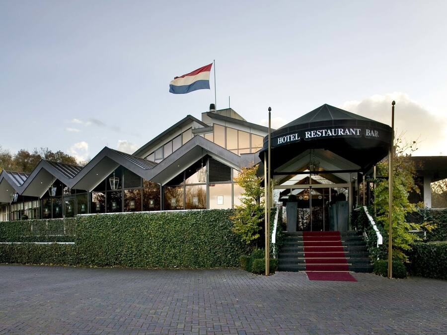 A modern hotel with a restaurant bar, a flag, and a red carpet entrance.
