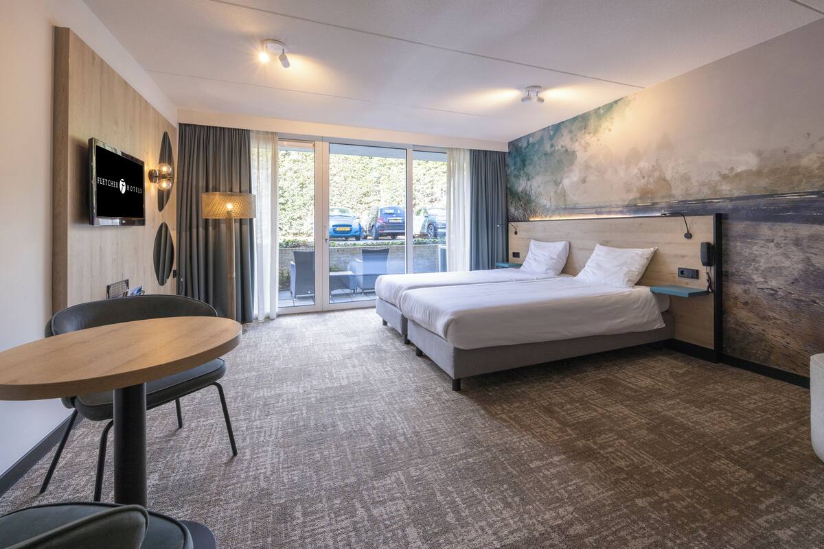A hotel room with a bed, a TV, a desk, and a view of parked cars outside.