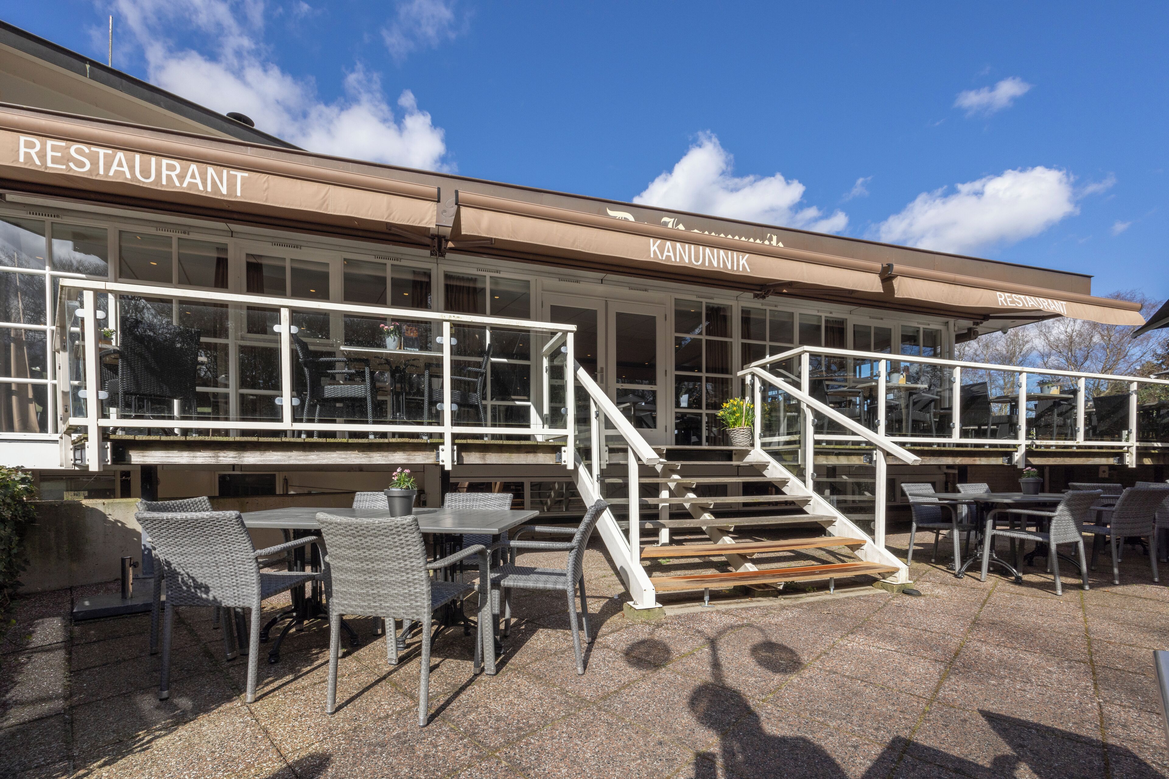 A restaurant with outdoor seating, a staircase leading to an upper level, and a clear blue sky.