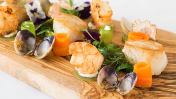 A wooden board with various seafood dishes, including shrimp, scallops, and mussels, garnished with herbs and vegetables.