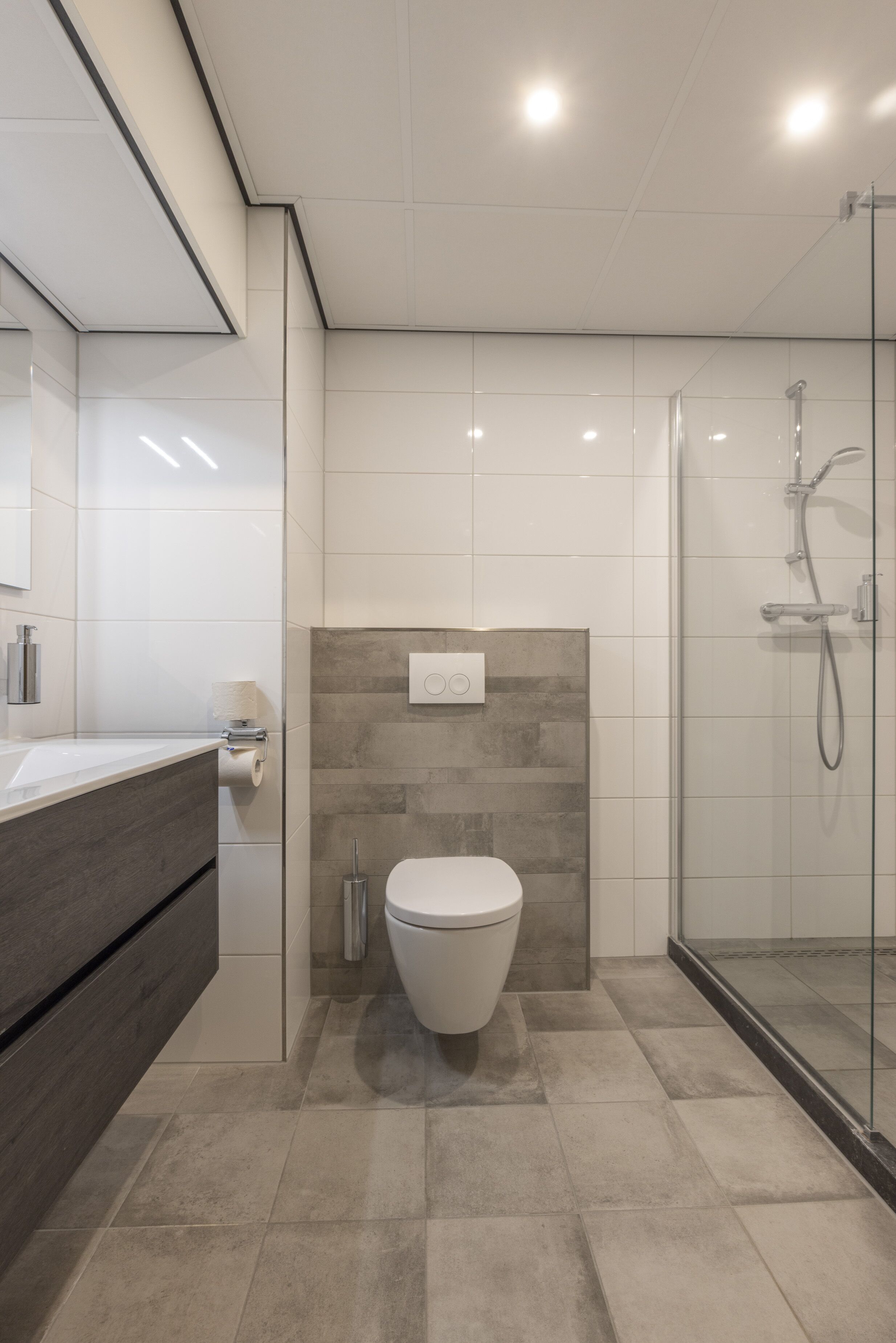 Een moderne badkamer met toilet, douche en een douchecabine met glazen wanden.