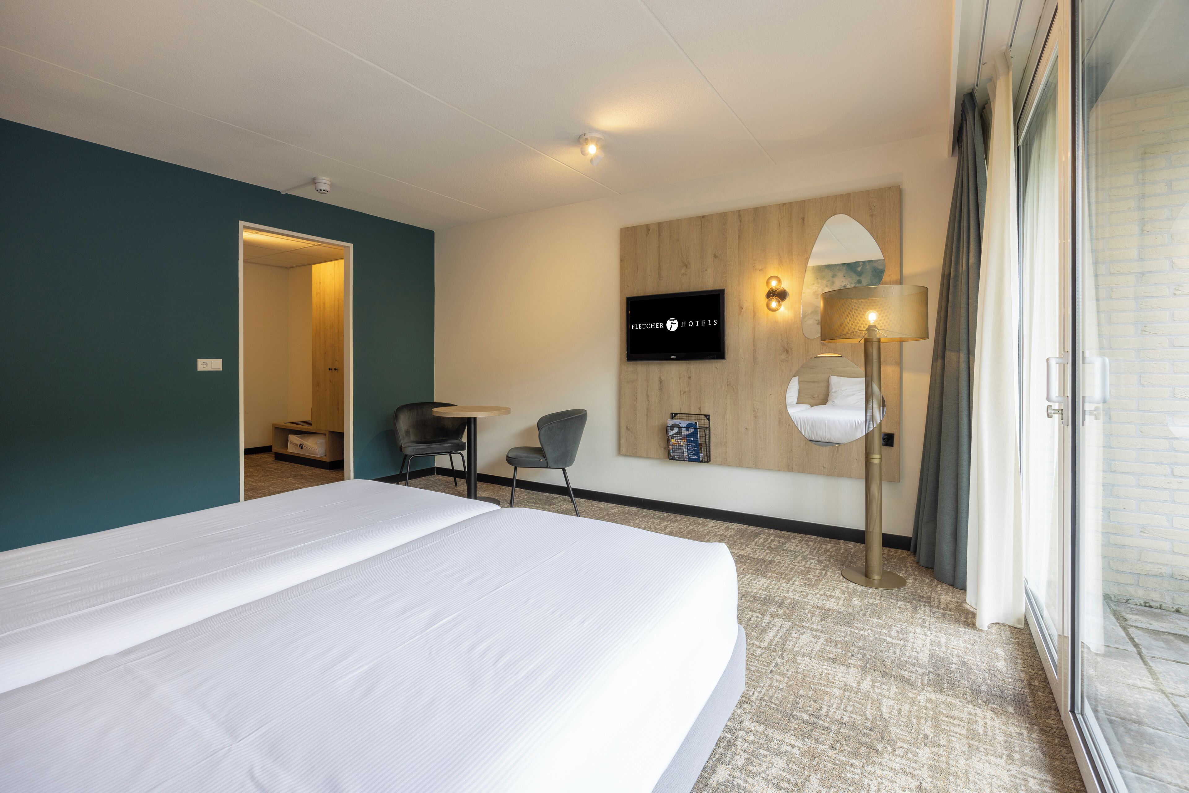 Hotelkamer met een groot bed, een bureau, een stoel, een aan de muur bevestigde televisie en een lamp.