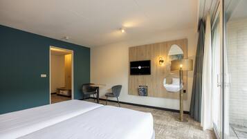 Hotelkamer met een groot bed, een bureau, een stoel, een aan de muur bevestigde televisie en een lamp.
