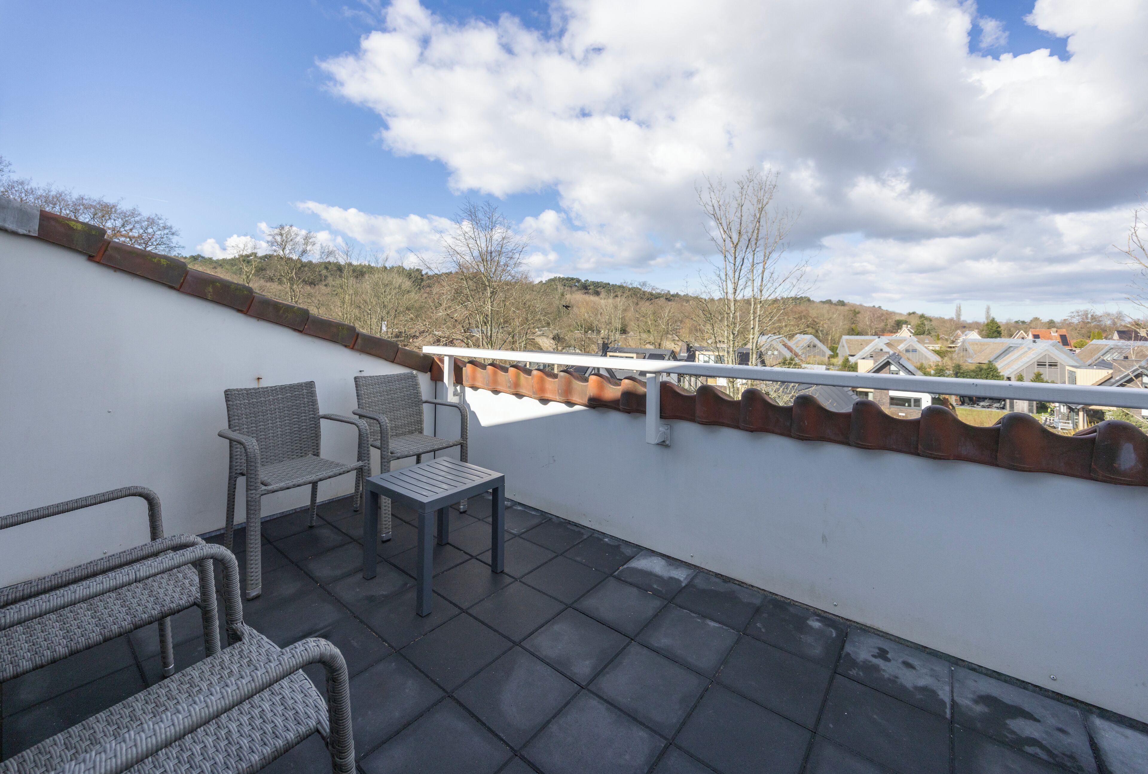 Eine Dachterrasse mit Korbmöbeln und Blick auf ein Wohngebiet.