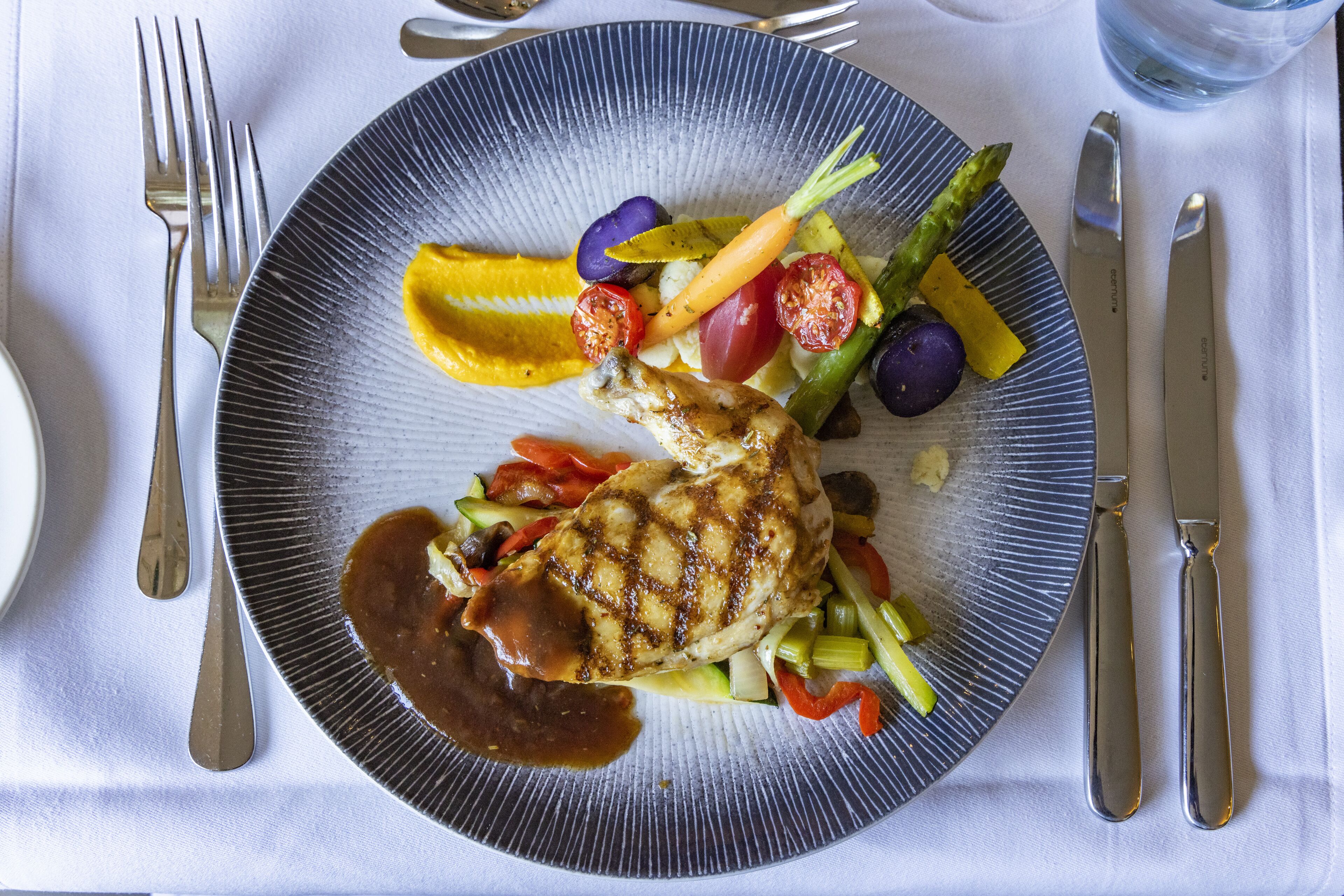 En tallerken med grillstegt kylling, grøntsager og sauce.