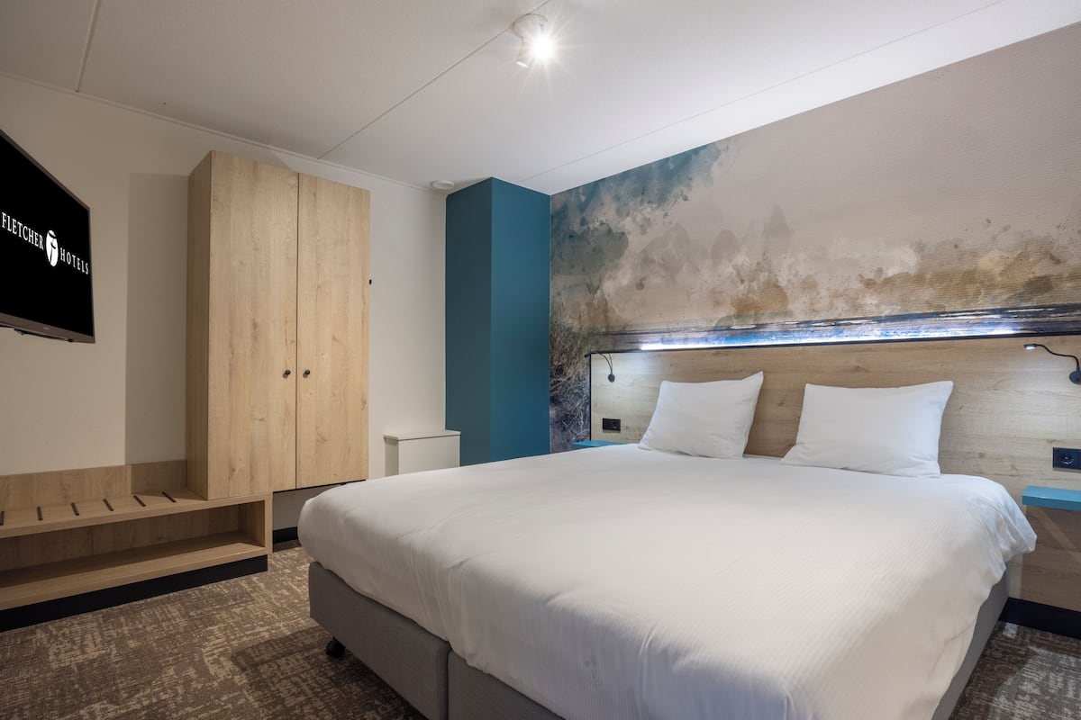 Habitació d'hotel moderna amb un llit gran, un armari de fusta i una televisió penjada a la paret.