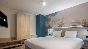 A modern hotel room with a large bed, wooden wardrobe, and a television on the wall.