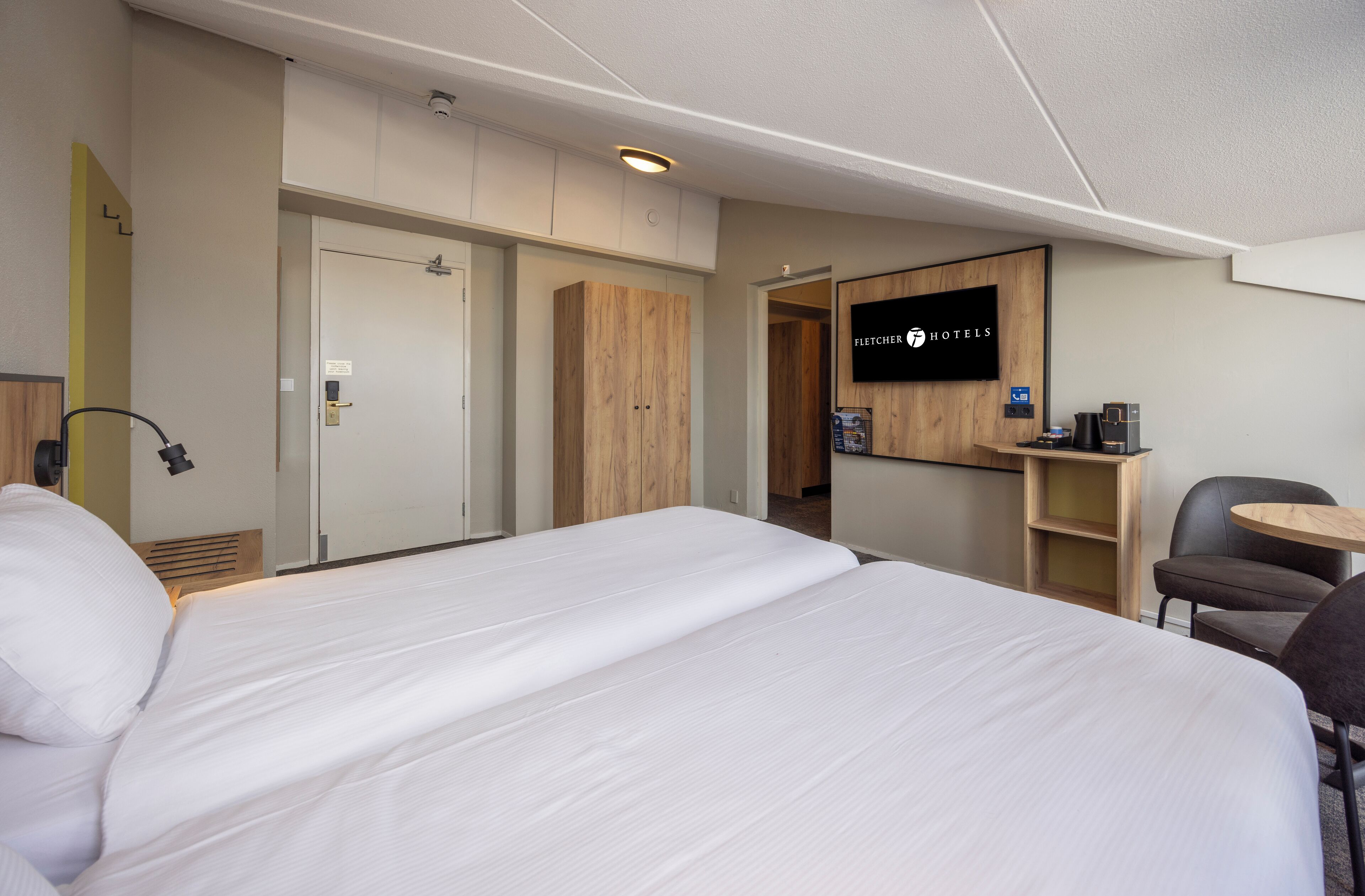 A hotel room with a bed, a desk, a chair, a television, and a wardrobe.