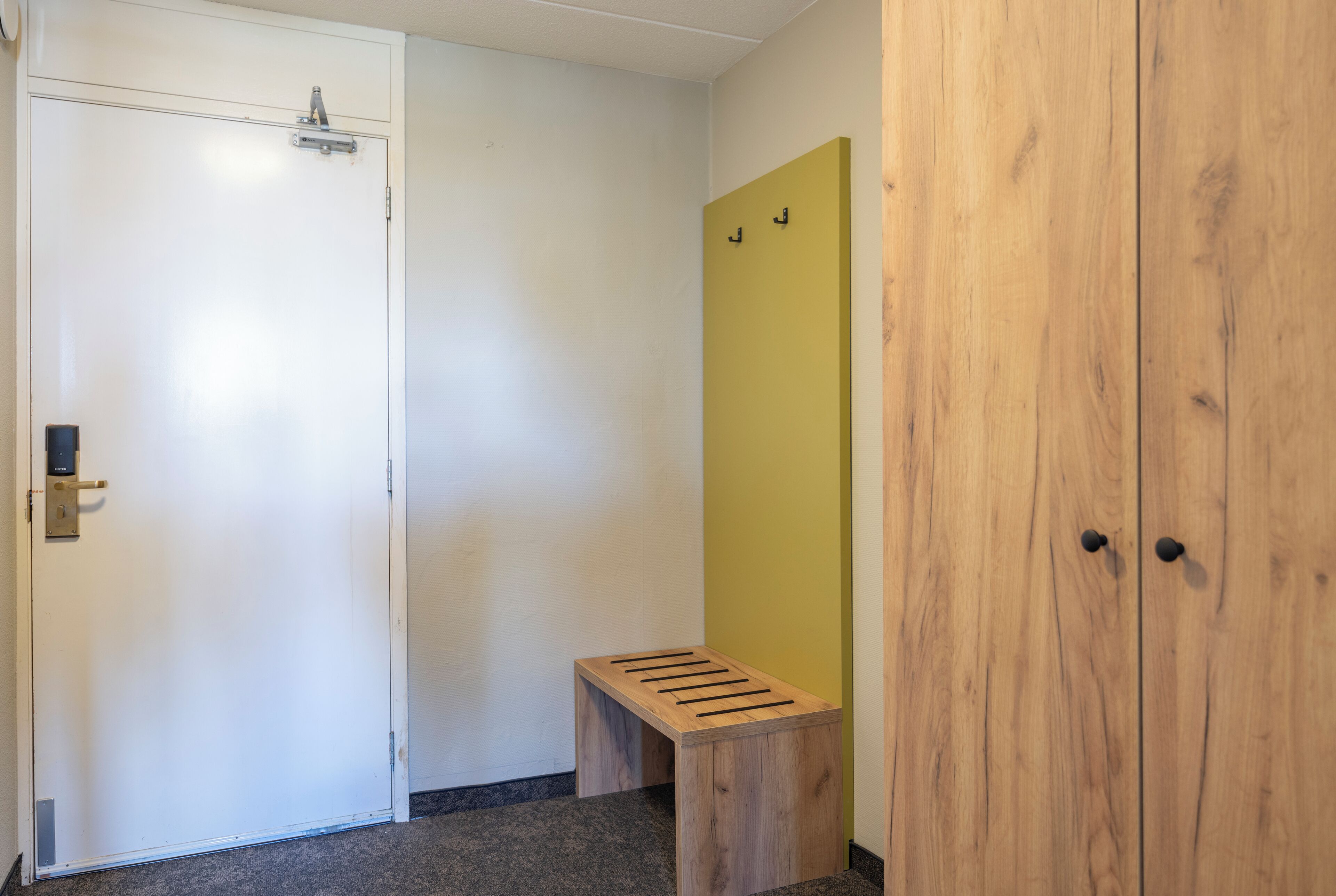 A hallway with a white door, a wooden bench, and a yellow wall.