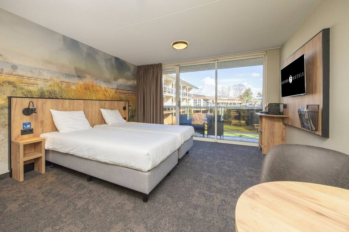 A hotel room with a bed, a desk, a chair, a TV, and a balcony with a view.