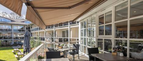 An outdoor patio with tables and chairs, a covered area with a roof, and large windows.