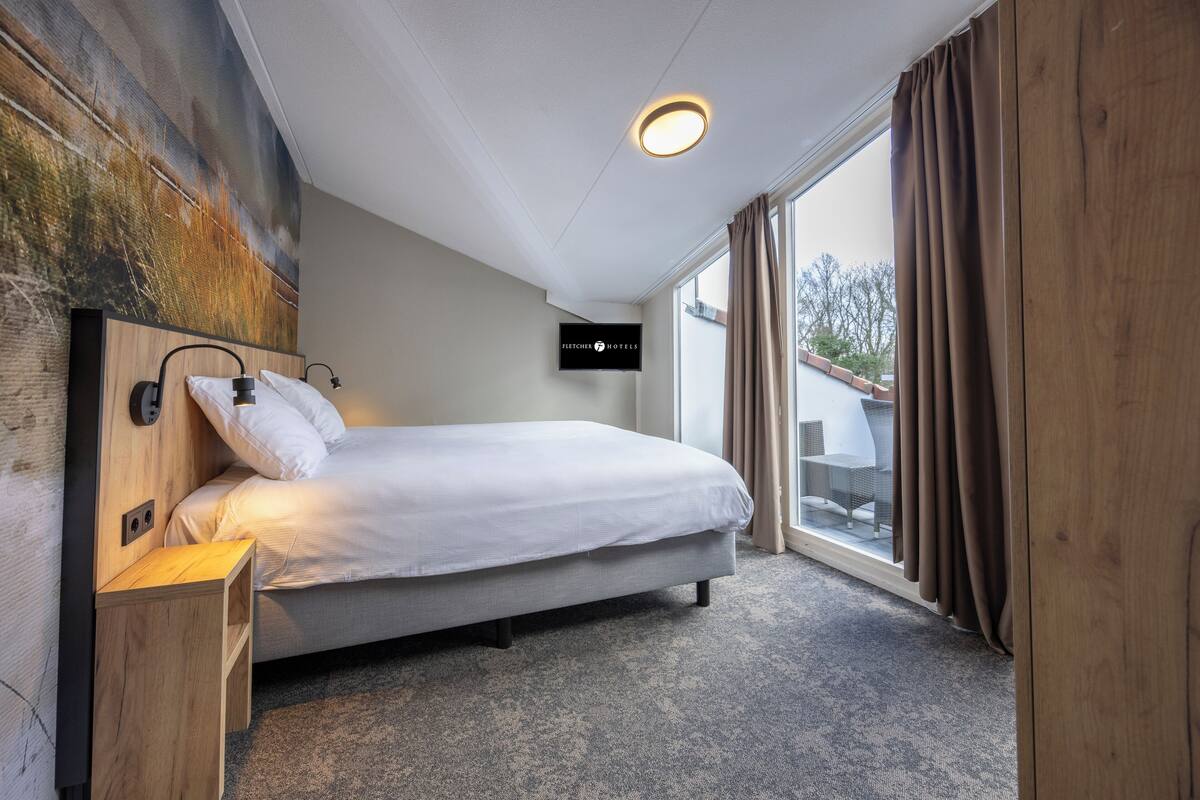Habitació d'hotel moderna amb un llit gran, un televisor de pantalla plana fixat a la paret i vistes a l'exterior a través d'un gran finestral.