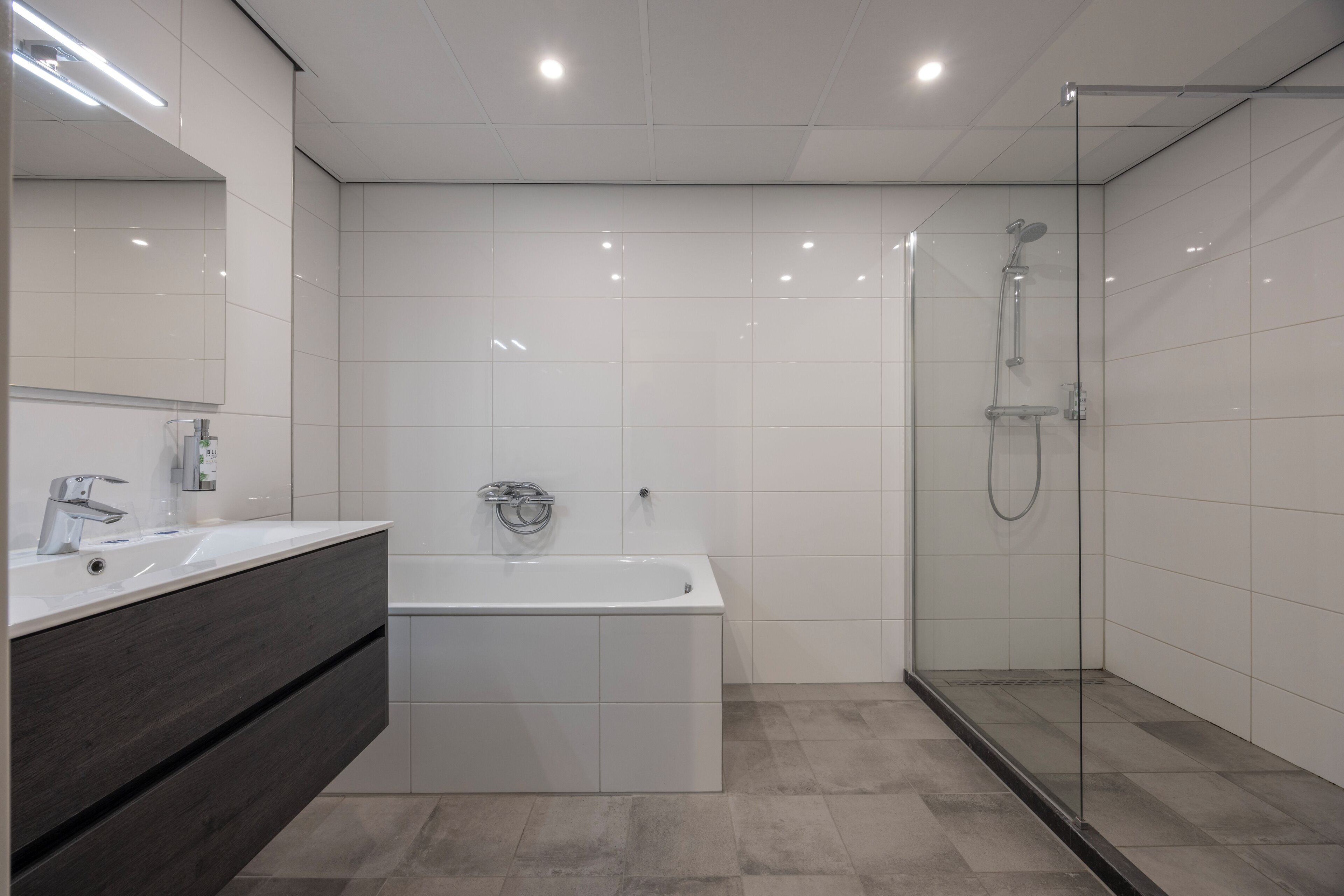 Ein modernes Badezimmer mit einer Badewanne, einer Duschkabine aus Glas und einem Waschtisch mit dunklen Holzschränken.