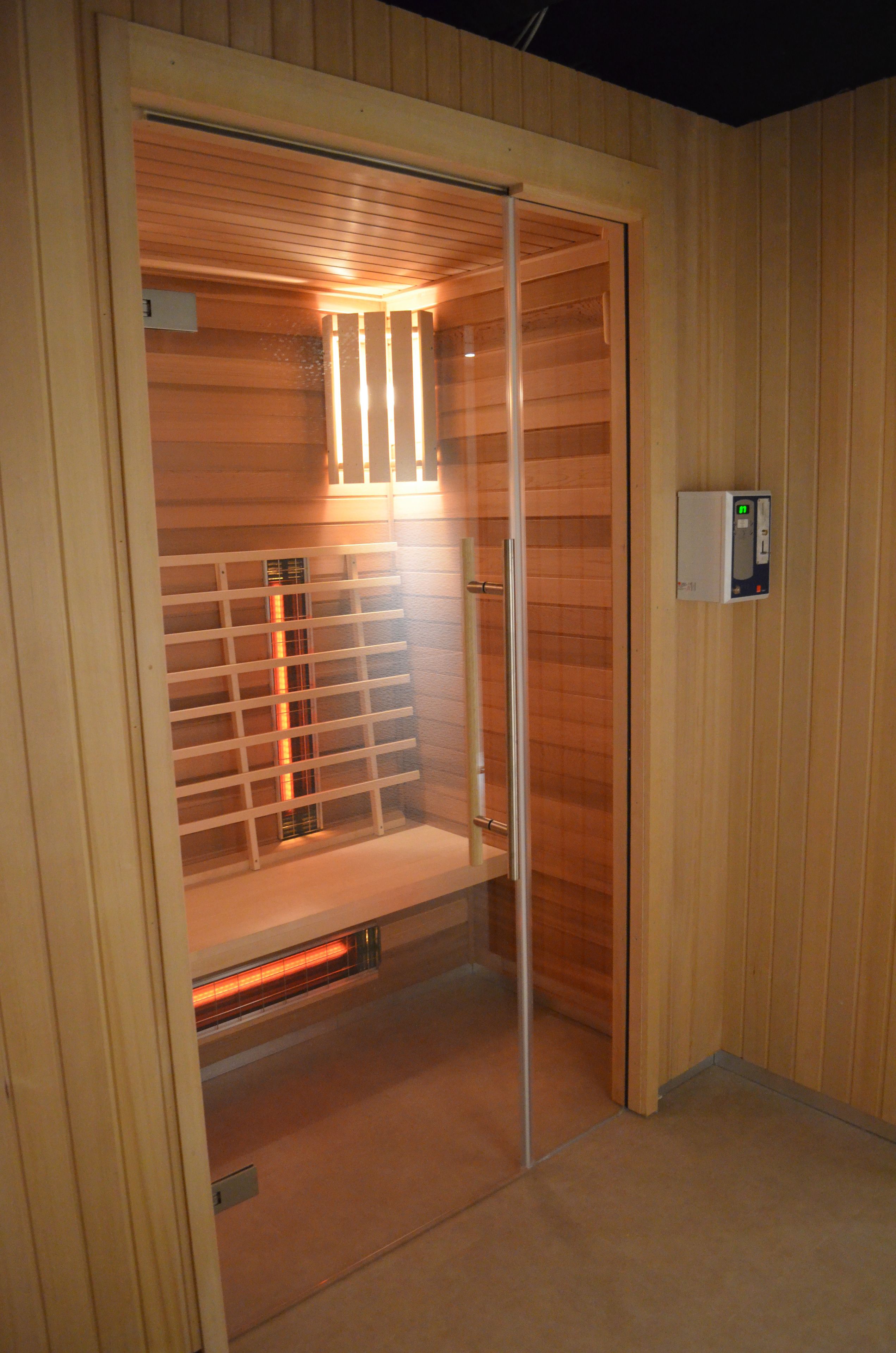 A sauna room with wooden walls, a bench, and a control panel.