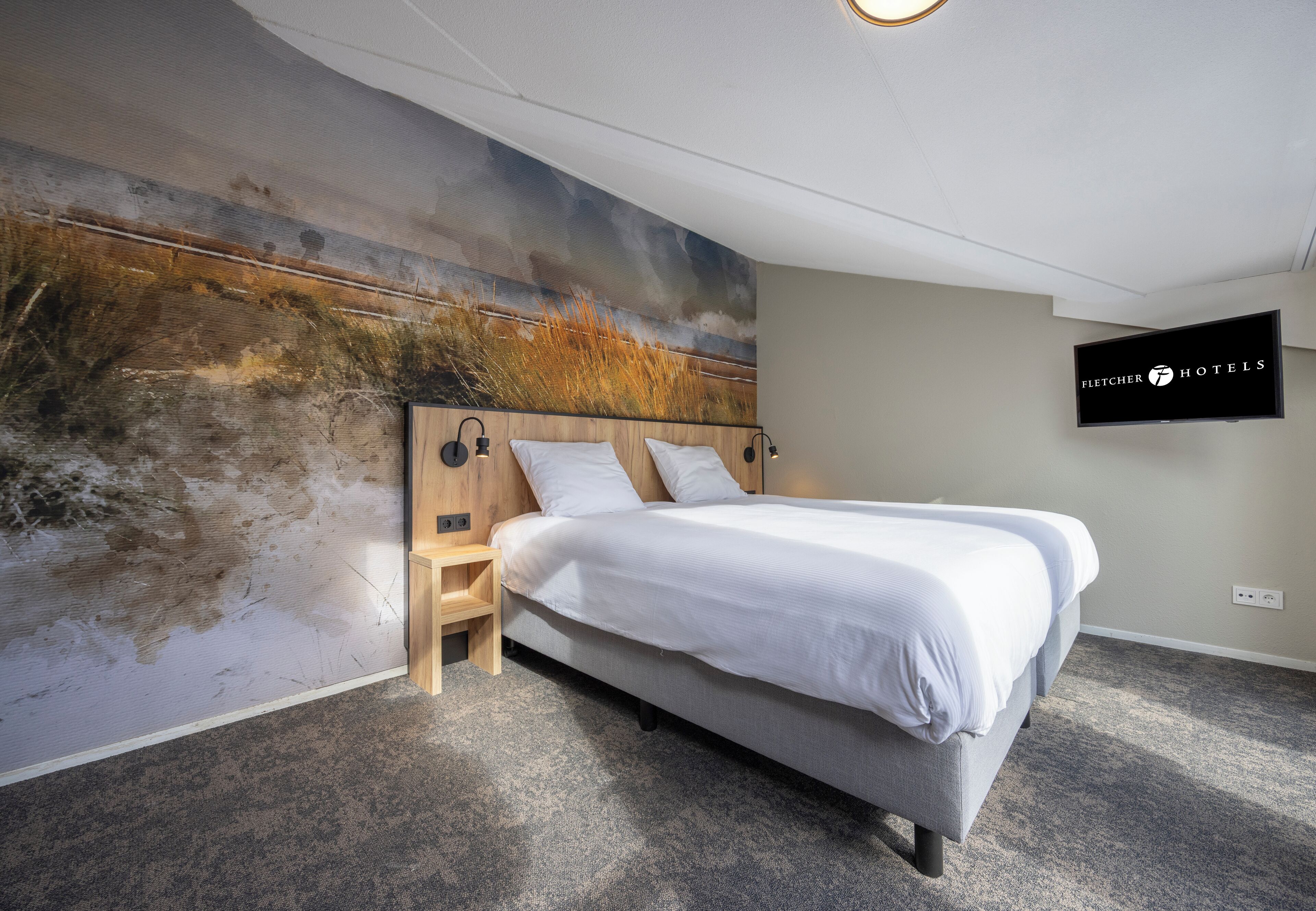 Una habitación de hotel moderna con una cama grande, un cabecero de madera, una mesita de noche pequeña, un televisor montado y un mural de pared con textura.