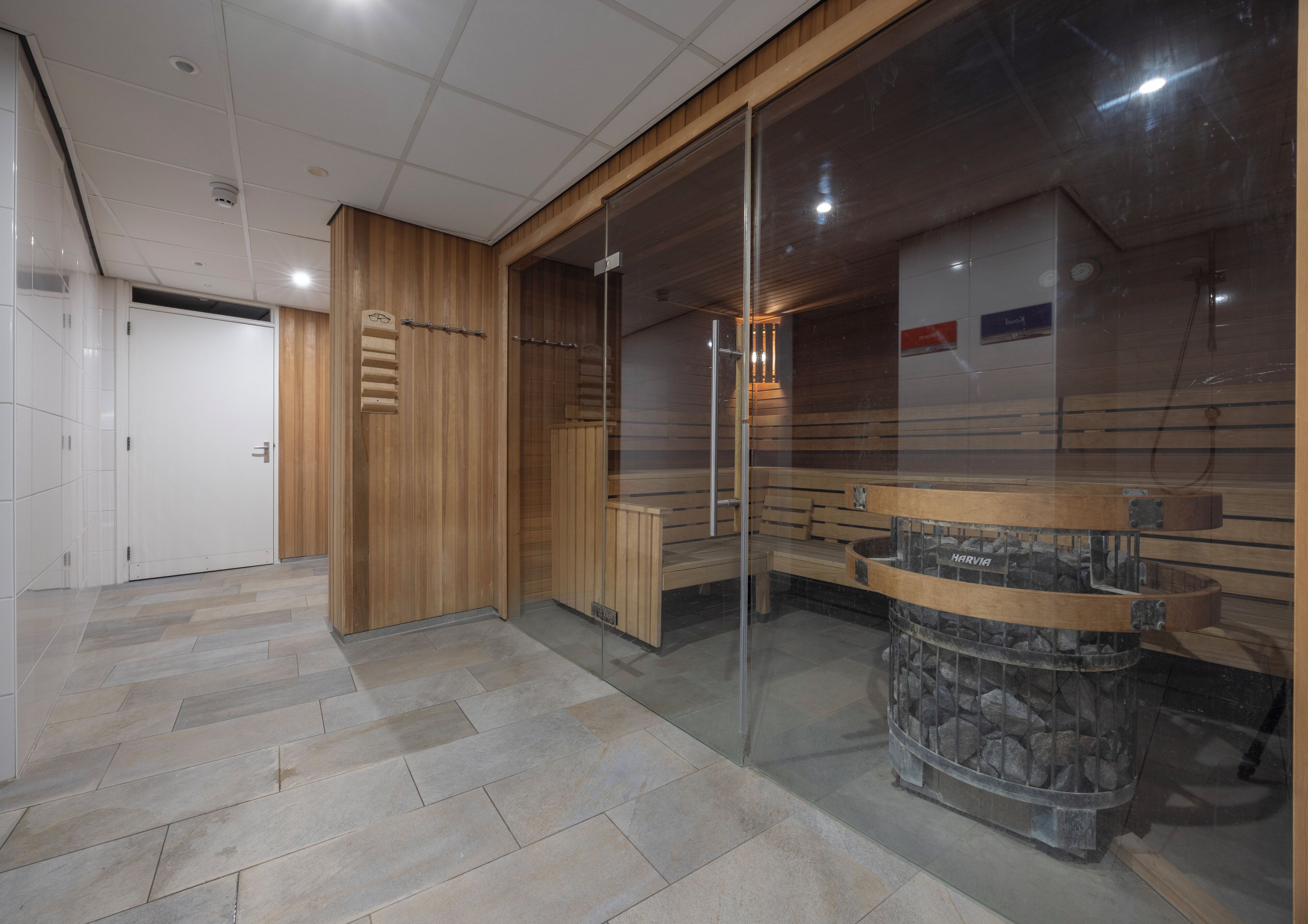 A modern sauna area with wooden benches, a glass partition, and a stone fire feature.