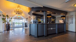 A hotel reception desk with a chandelier, a clock, and a large potted plant. - Fletcher Hotel-Restaurant Jan van Scorel (Schoorl)
