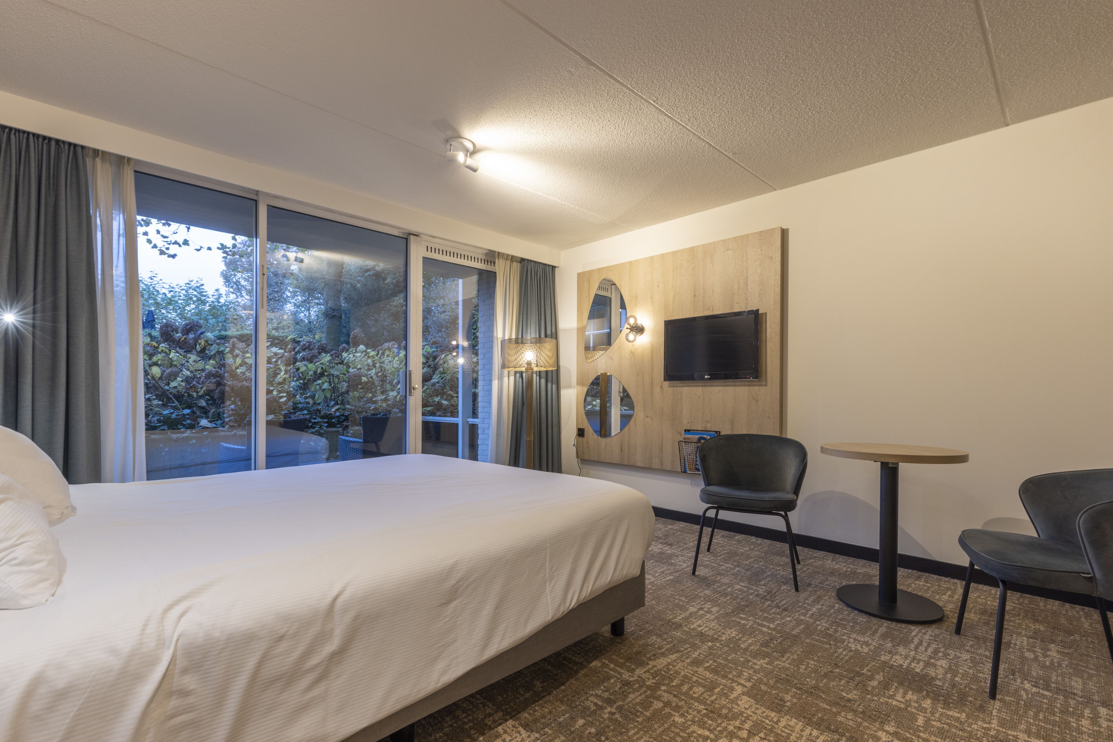 A hotel room with a large bed, a TV mounted on the wall, a small table, and a chair.