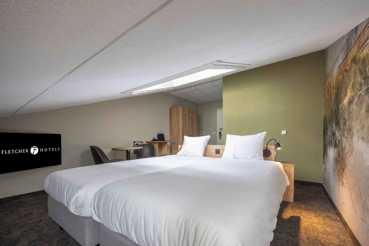 A hotel room with a large bed, a desk, a chair, a small table, and a mirror.