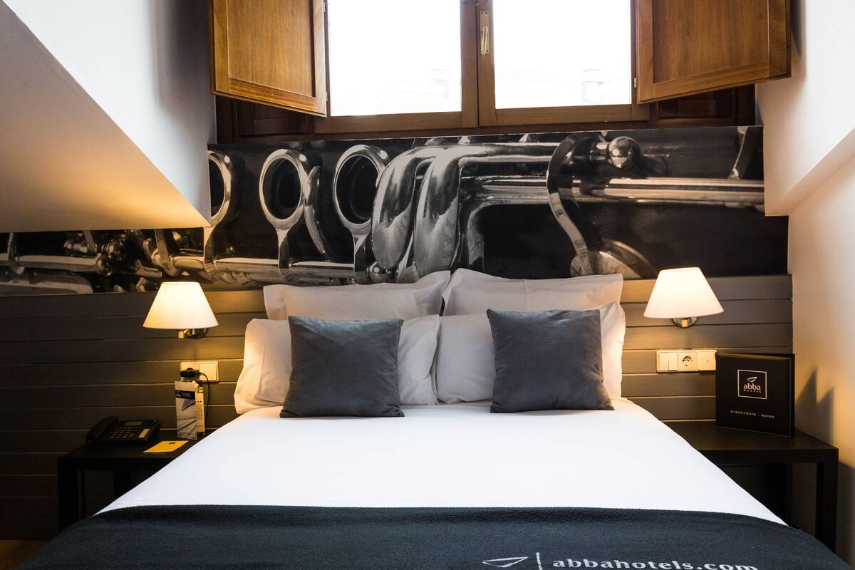 Een hotelkamer met een bed, twee bedlampen, een nachtkastje met een telefoon en een aan de muur hangend schilderij.