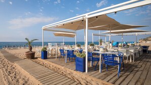 Un espacio al aire libre con mesas y sillas, una terraza de madera y vistas a la playa y al océano.