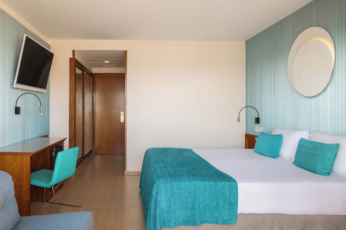 Habitación de hotel con cama, escritorio, silla, televisor y espejo en la pared.