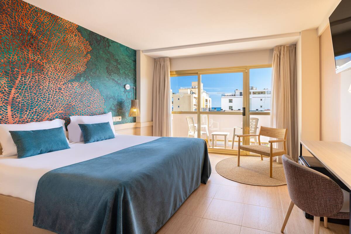 Una habitación de hotel con una cama grande, un escritorio y vistas a edificios a través de la ventana.