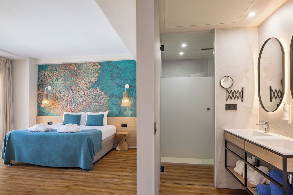 A modern hotel room with a large bed, a bathroom with a mirror and sink, and a wall with a decorative pattern.