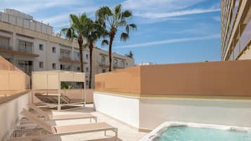 Terraza en la azotea con jacuzzi, sillas de descanso y palmeras.