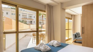 Habitación de hotel con una cama, un edredón azul, dos toallas blancas, un sofá gris y vistas al balcón exterior.