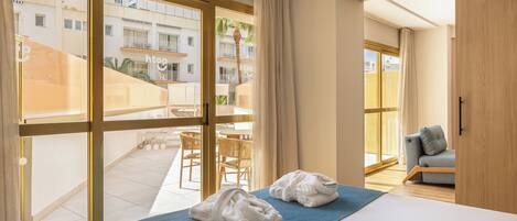Een hotelkamer met een bed, een blauwe spreidek, twee witte handdoeken, een grijze bank en uitzicht op het balkon.