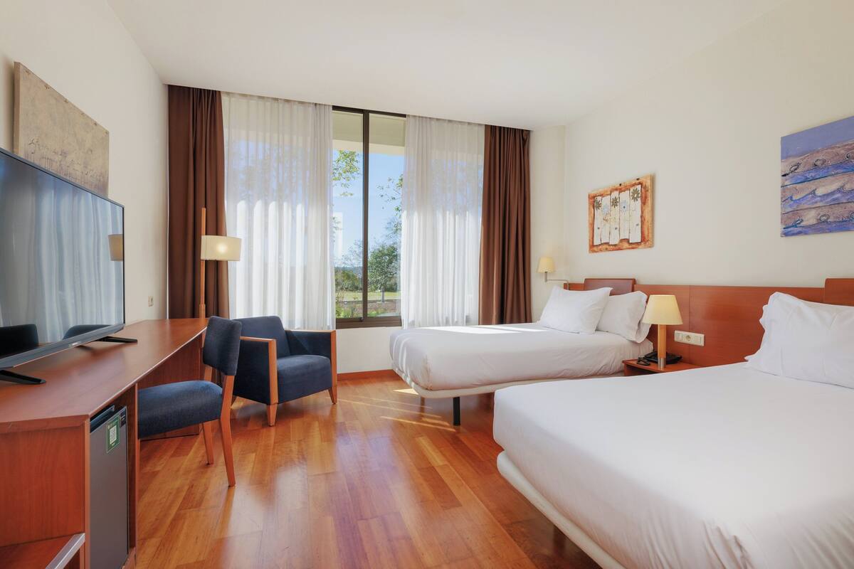 A hotel room with a large bed, a desk with a television, and a chair. There are two bedside tables with lamps.
