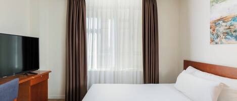 A hotel room with a bed, a TV on a wooden desk, and curtains.