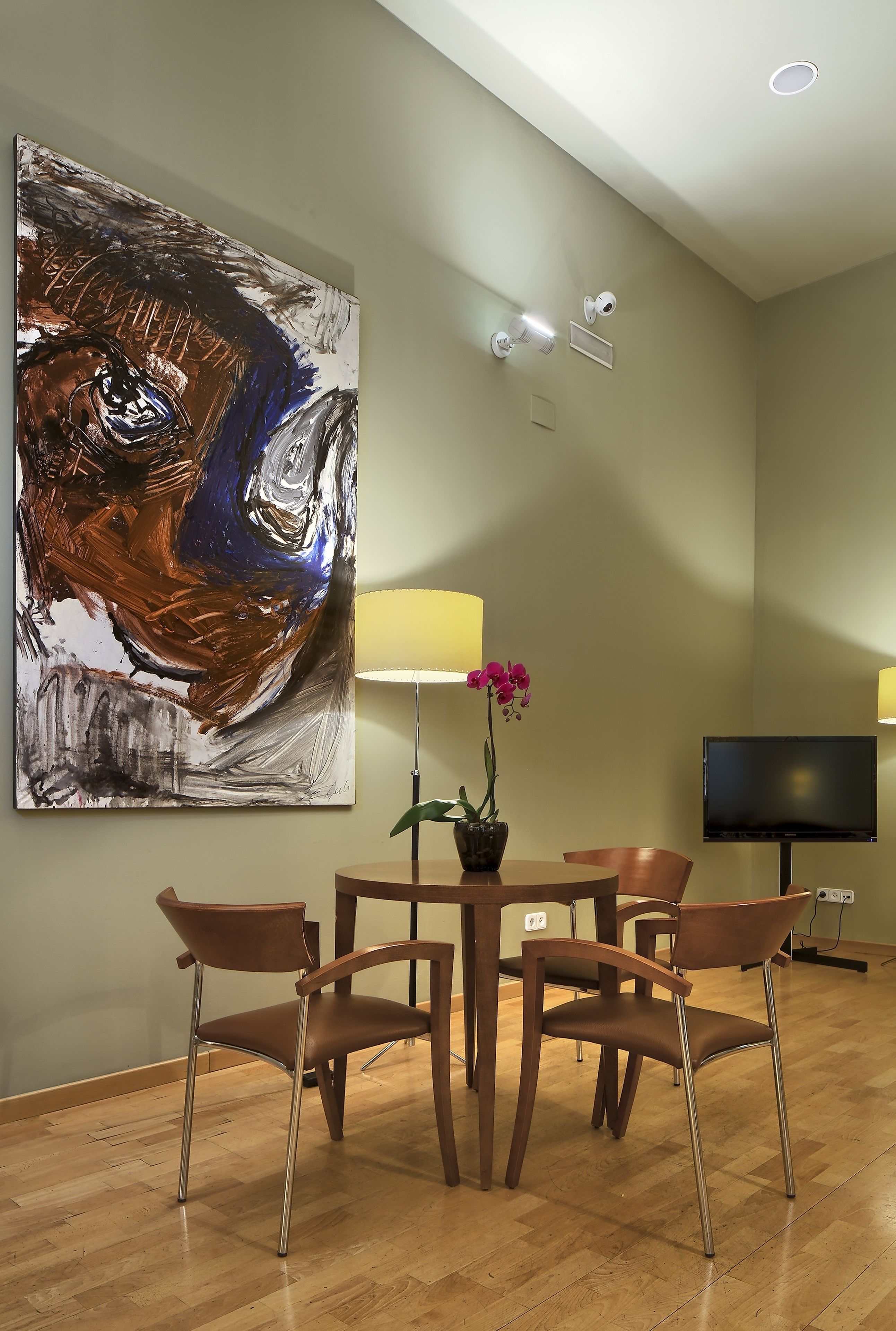 Un salón moderno con un cuadro abstracto grande, una mesa de comedor con cuatro sillas, un televisor y una orquídea en maceta.