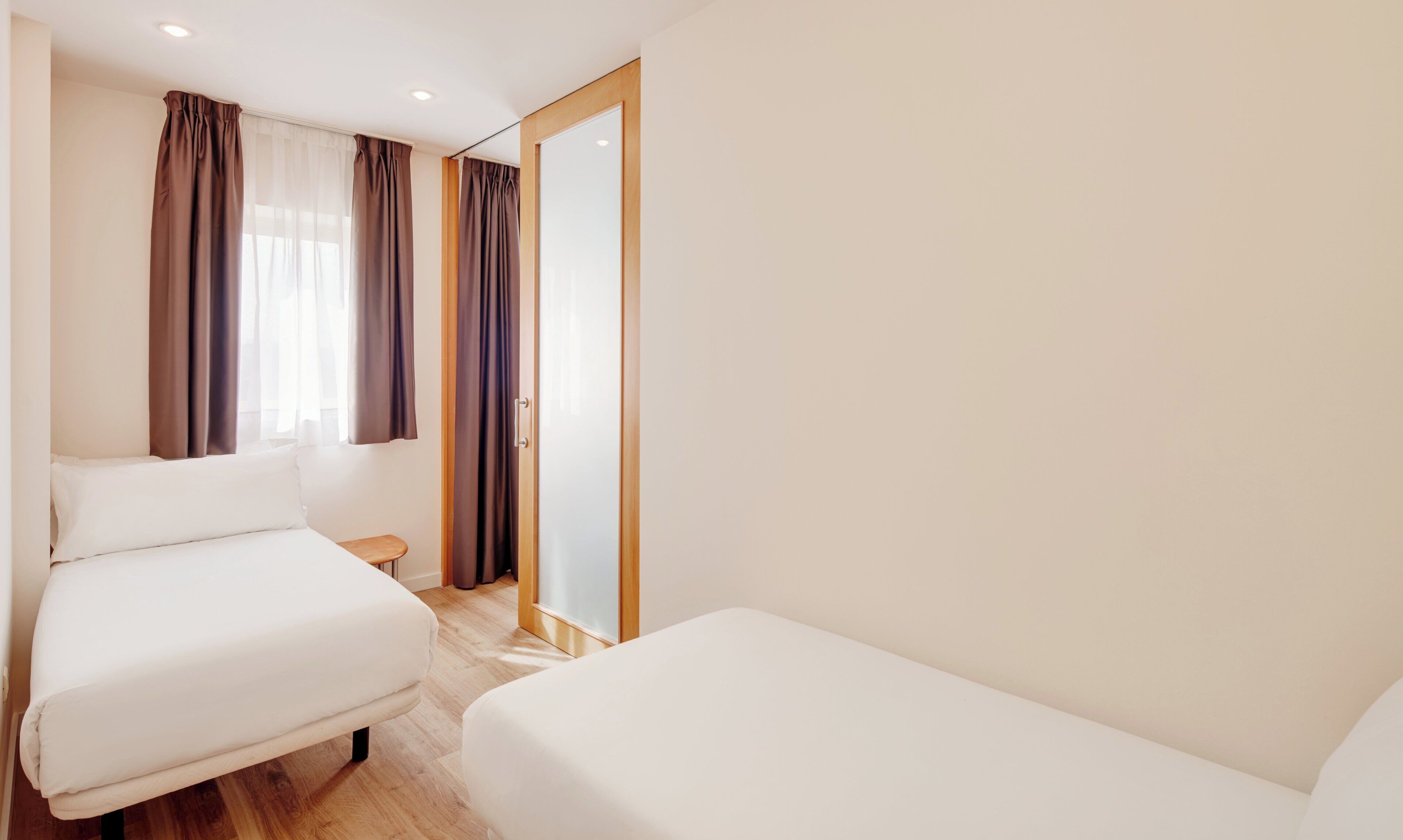 Habitación de hotel con dos camas individuales, piso de madera, una mesita de noche pequeña y una puerta corredera.