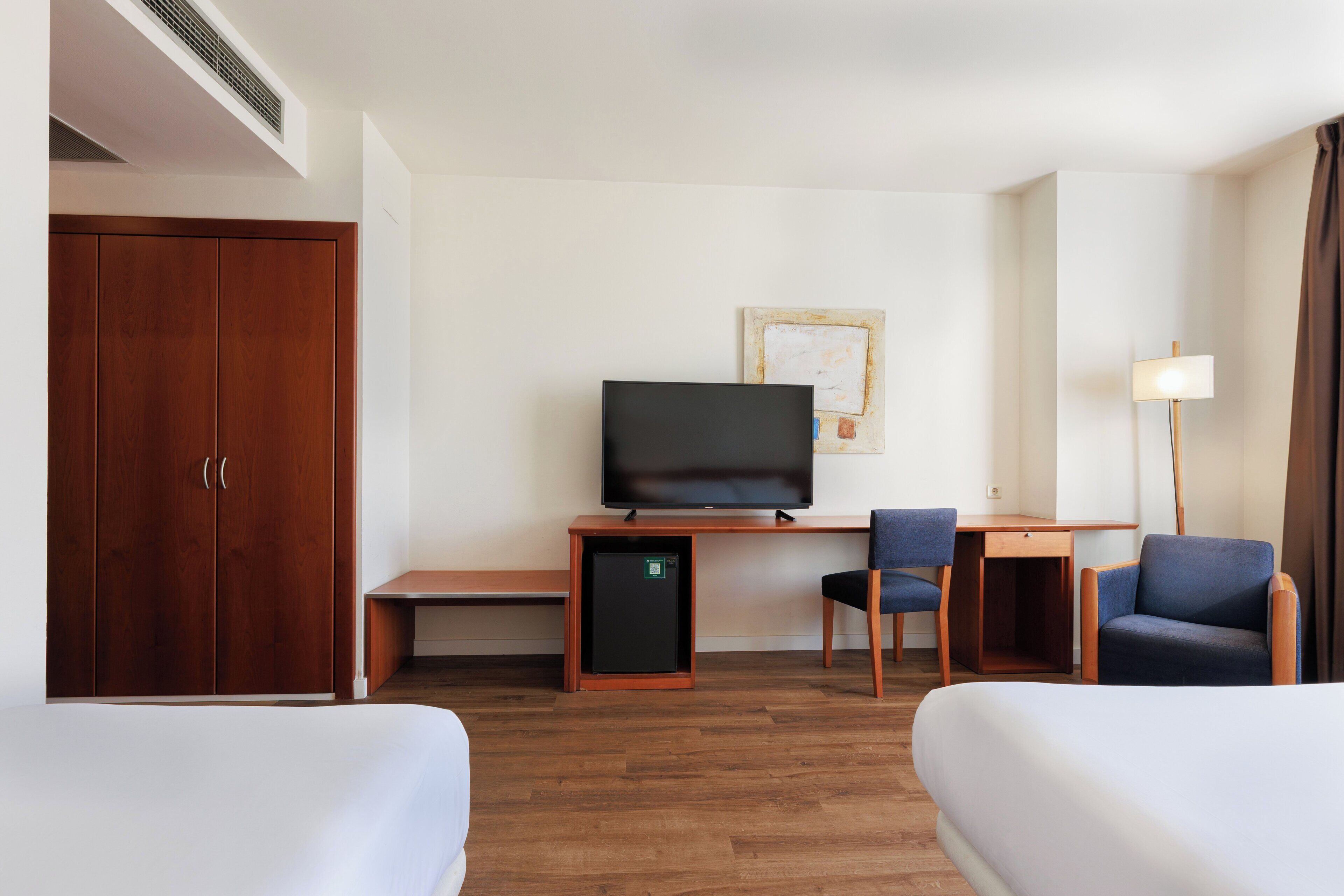 Een hotelkamer met twee bedden, een bureau met een televisie, een kleine koelkast en een lamp.